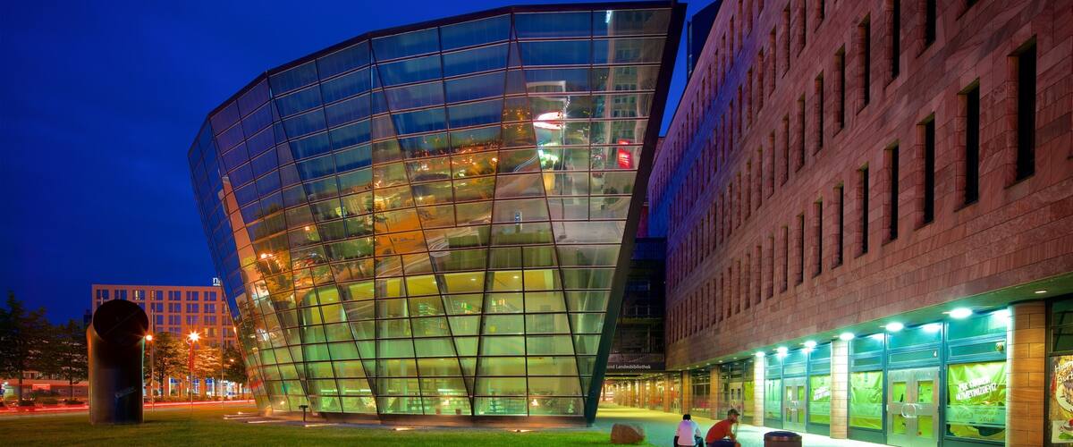 A modern glass building with a curved facade, surrounded by a grassy area and a brick building.