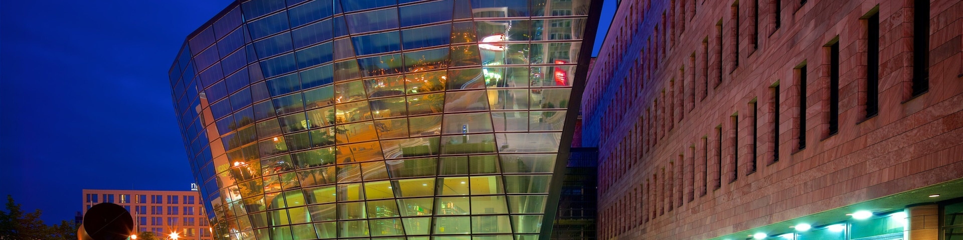 A modern glass building with a curved facade, surrounded by a grassy area and a brick building.