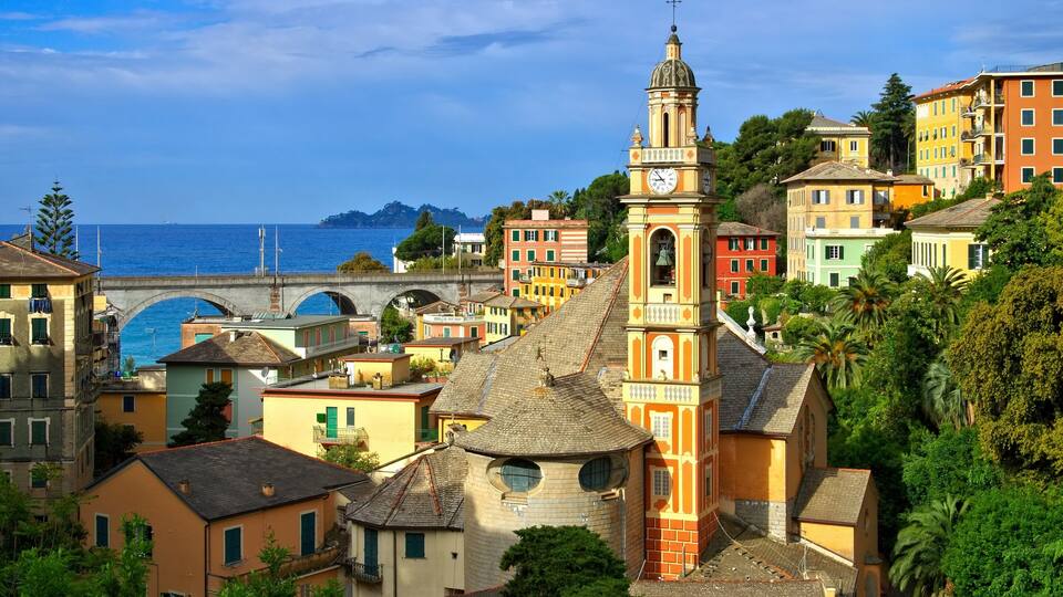 A coastal town with colorful buildings, a prominent church tower, and a bridge over the sea.