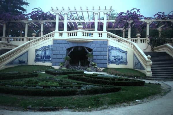 A garden with a central fountain, a bridge, and manicured hedges.