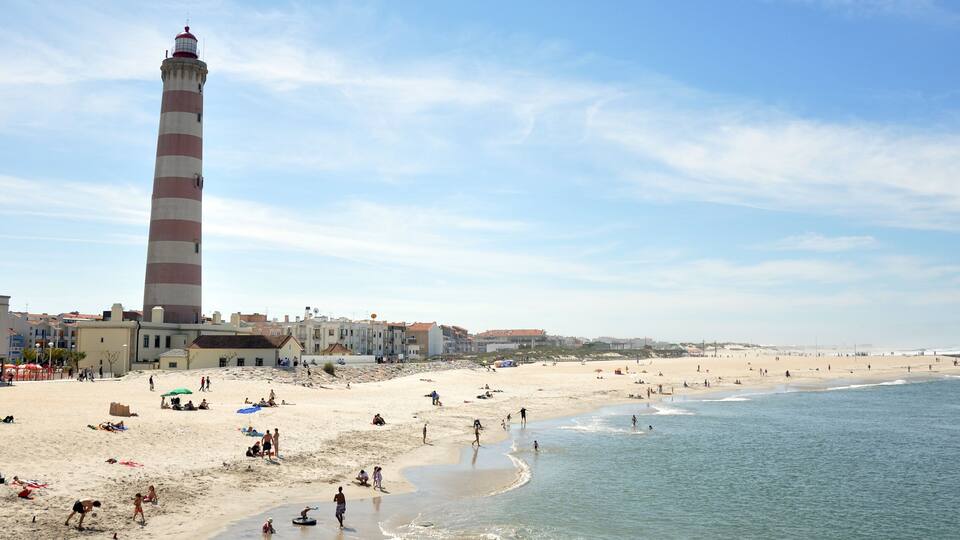 A beach with a tall lighthouse, sandy shore, and ocean waves.