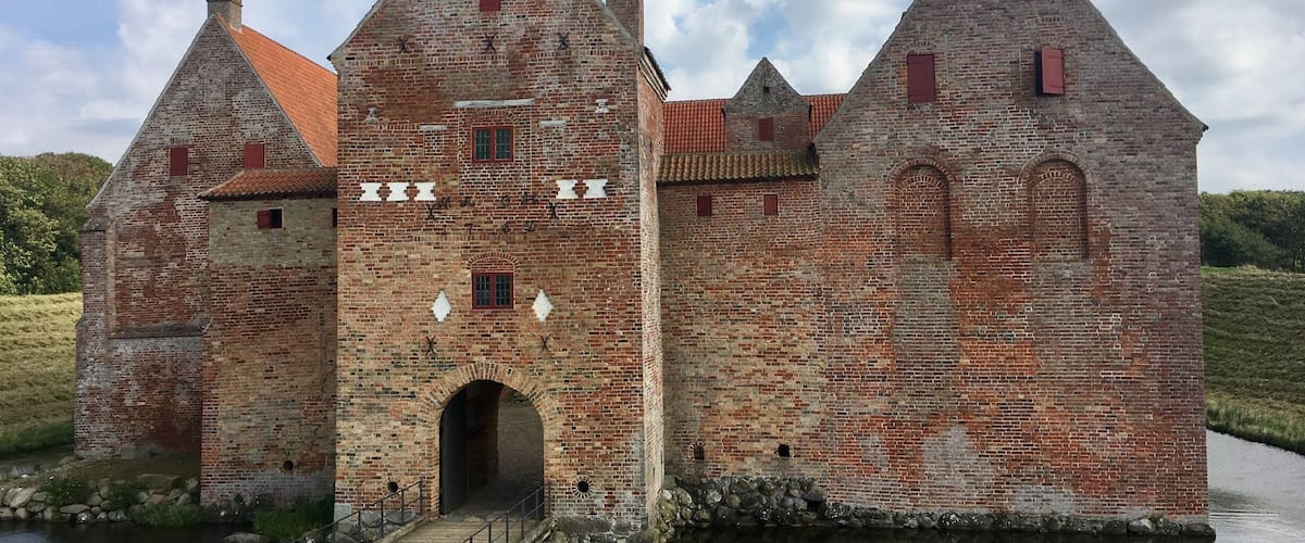 A historic brick castle with a moat and a wooden bridge.