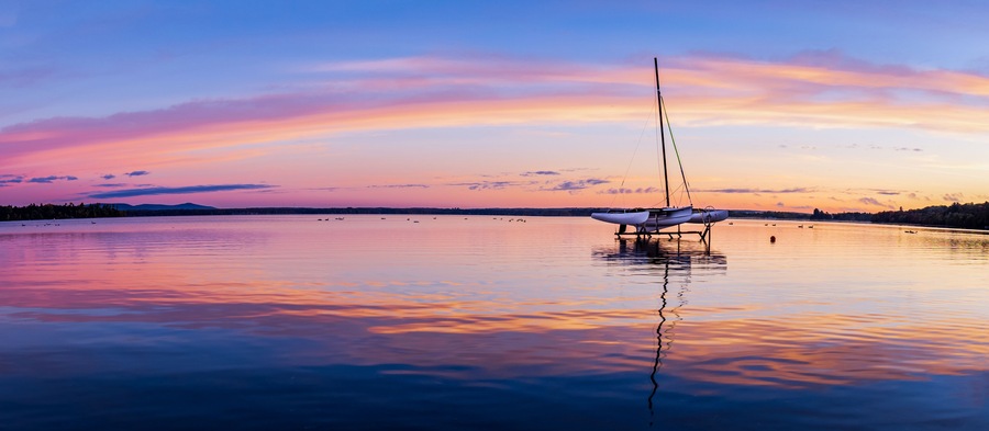 Un lago tranquilo al atardecer con un velero anclado en el centro.