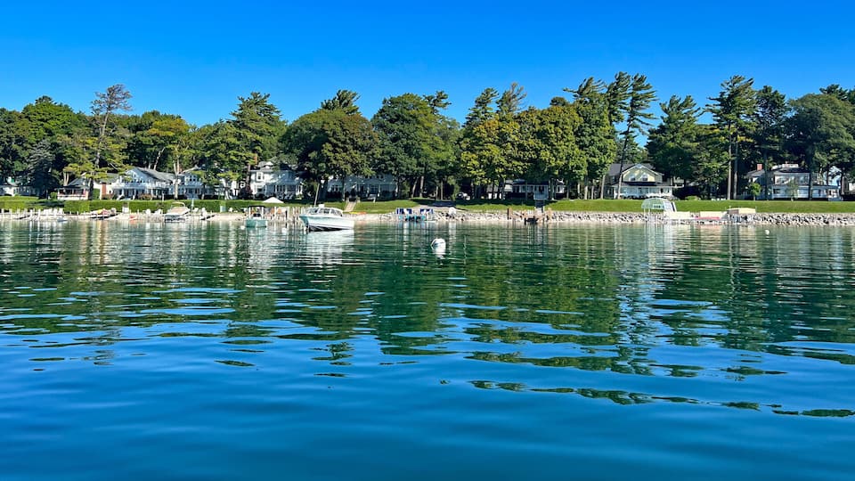 A calm lake with boats, a swan, and houses along the shore.