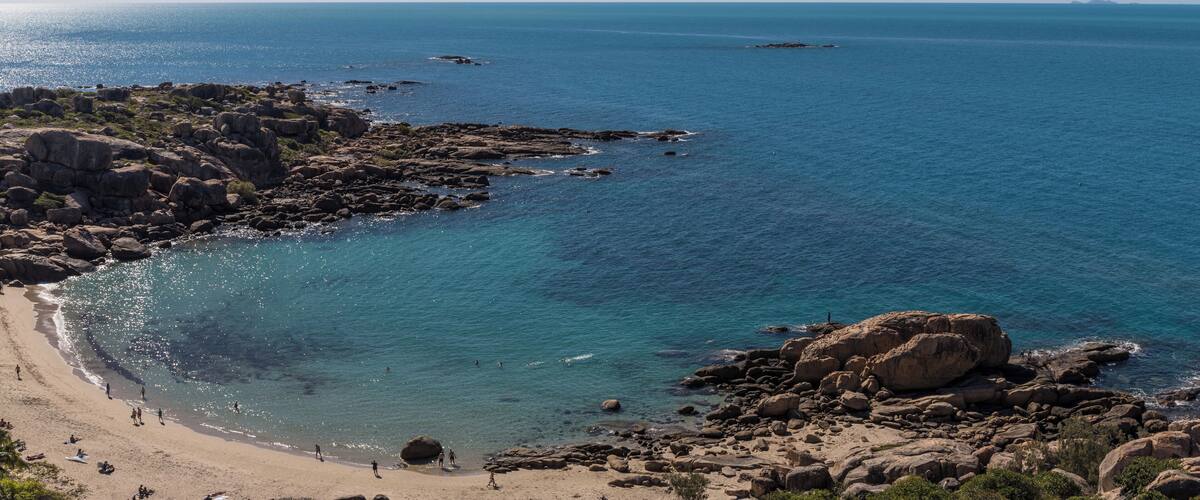 A rocky beach with clear blue water and people sunbathing.