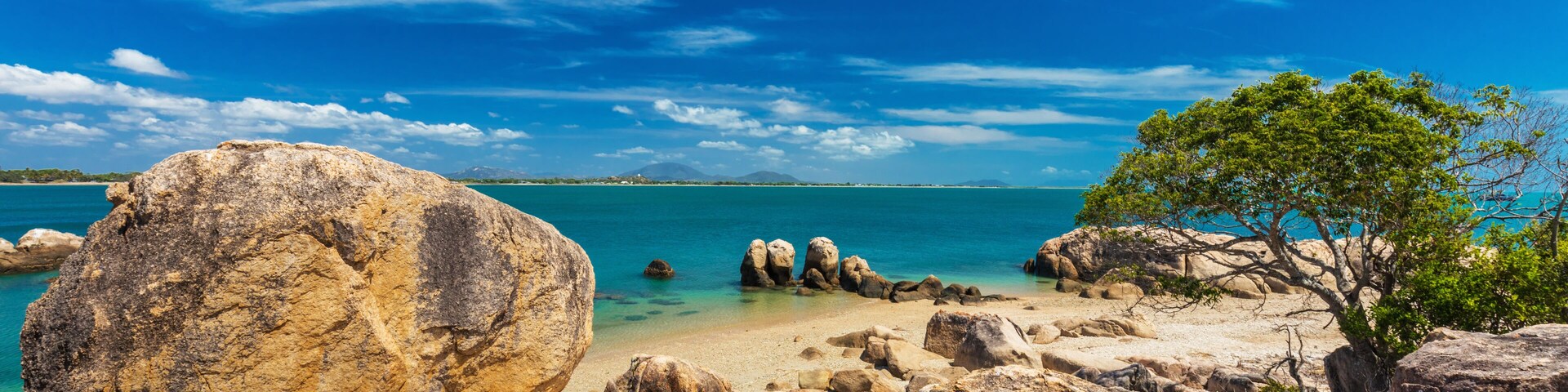 A rocky beach with large boulders, clear turquoise water, and a clear blue sky.