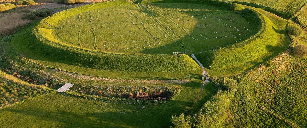 Un'ampia distesa circolare con un sentiero centrale, circondata da dolci colline e fitte foreste.