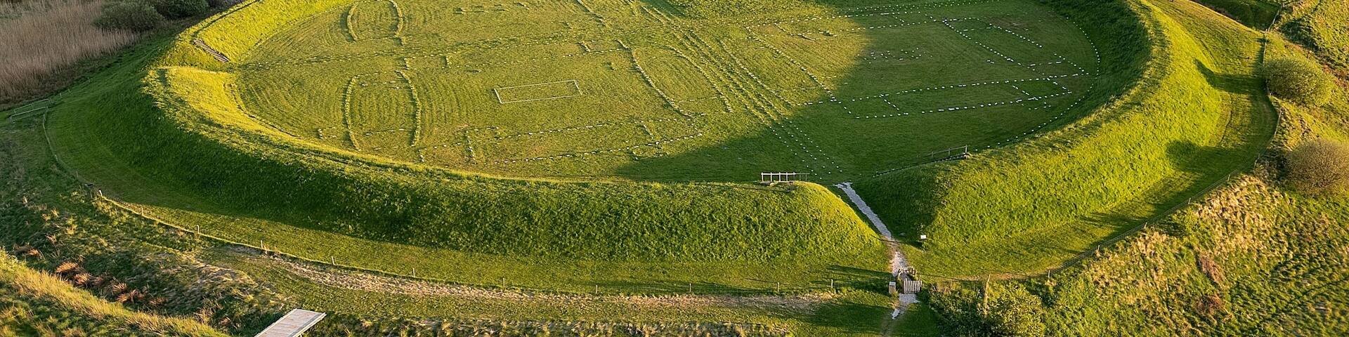 A large circular field with a central path, surrounded by rolling hills and dense forests.