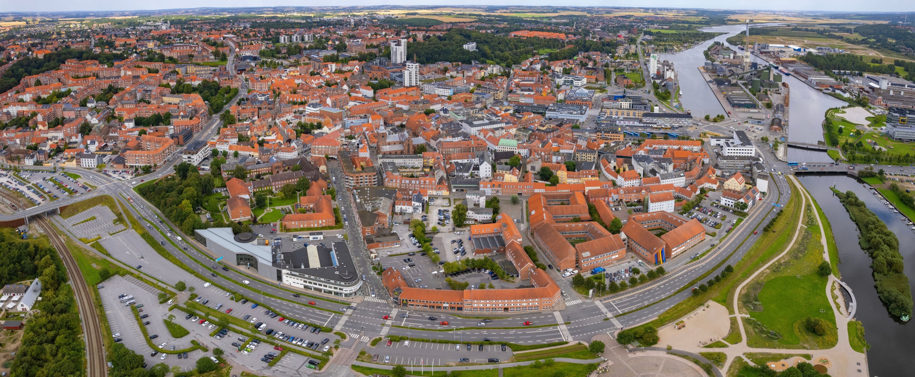 An aerial view of a city with a river, a roundabout, and a mix of red-roofed buildings.