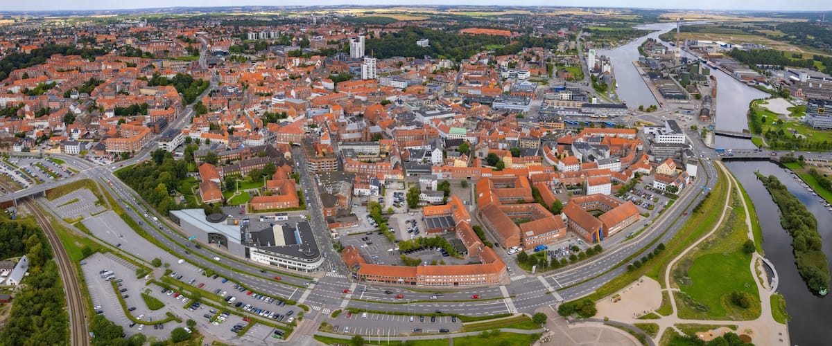 An aerial view of a city with a river, a roundabout, and a mix of red-roofed buildings.