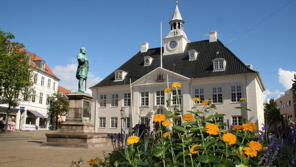 A historic building with a statue in front, surrounded by vibrant flowers.