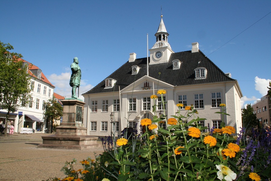 A historic building with a statue in front, surrounded by vibrant flowers.
