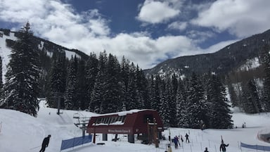 Um teleférico, um edifício vermelho com a inscrição "Groove Mountain Express 10" e árvores cobertas de neve.