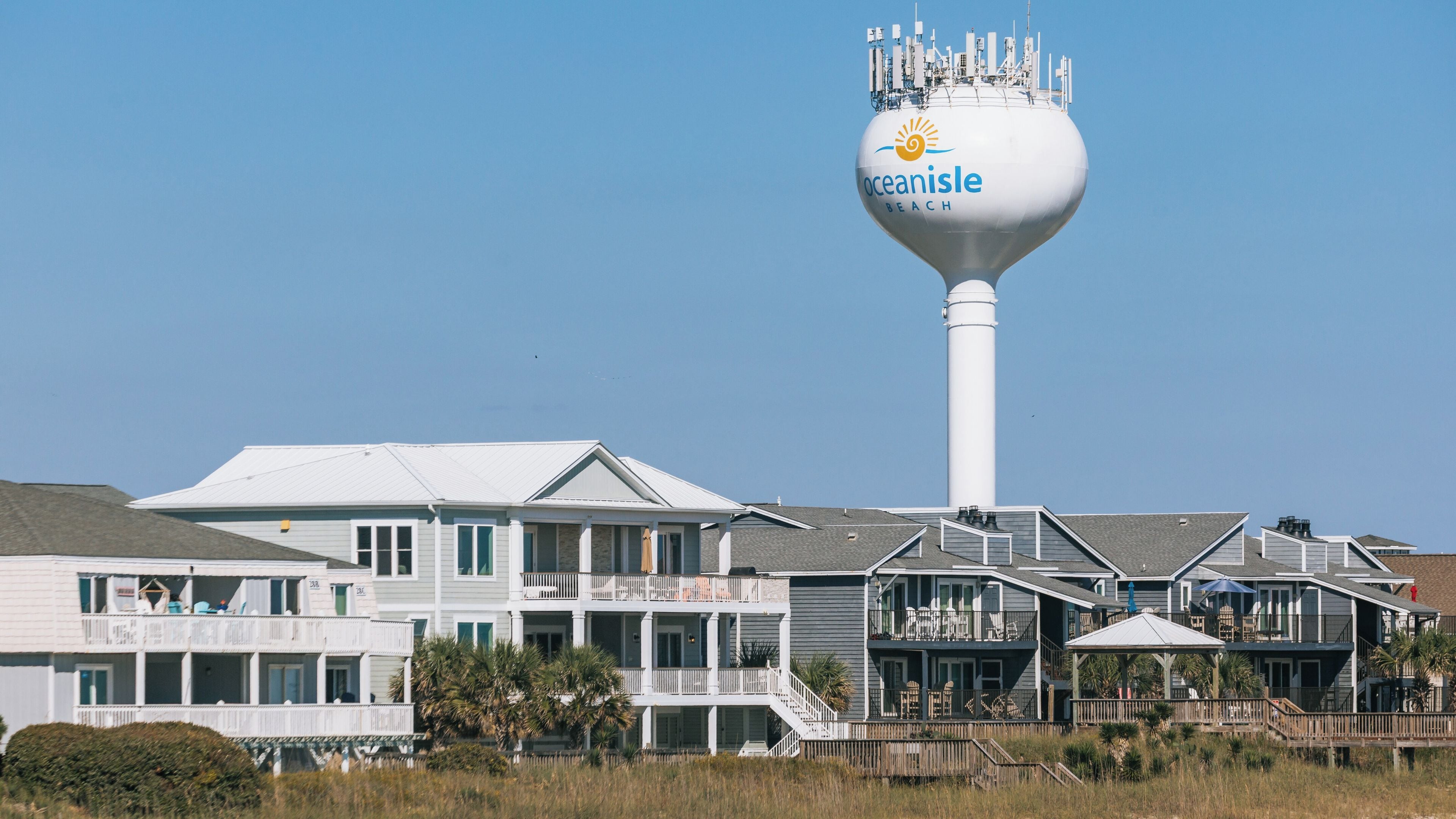 A coastal residential area with a prominent water tower labeled 'Oceanisle Beach' and a series of multi-story houses with balconies.