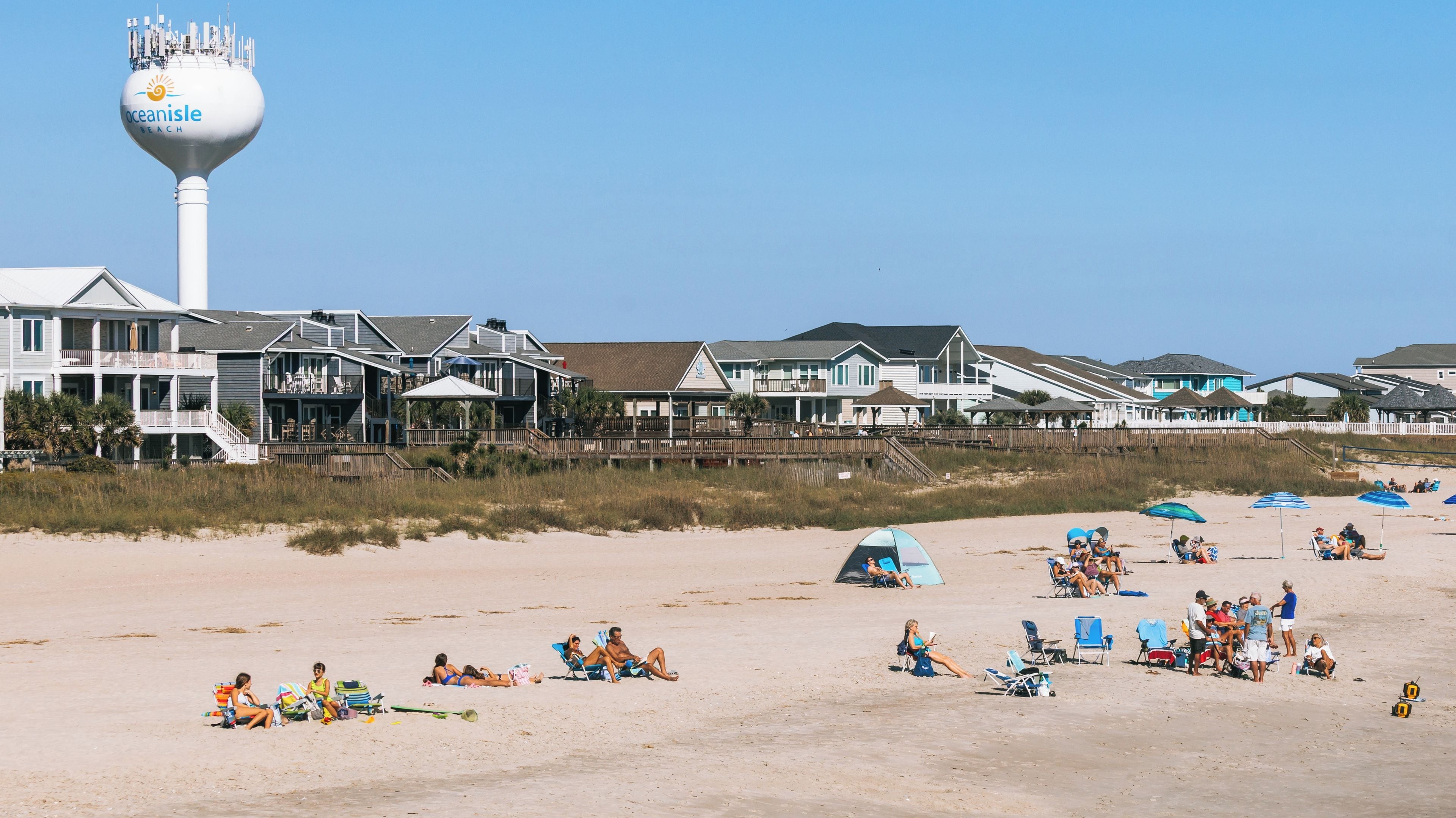 A beach with beach houses, a water tower, and people relaxing on the sand.