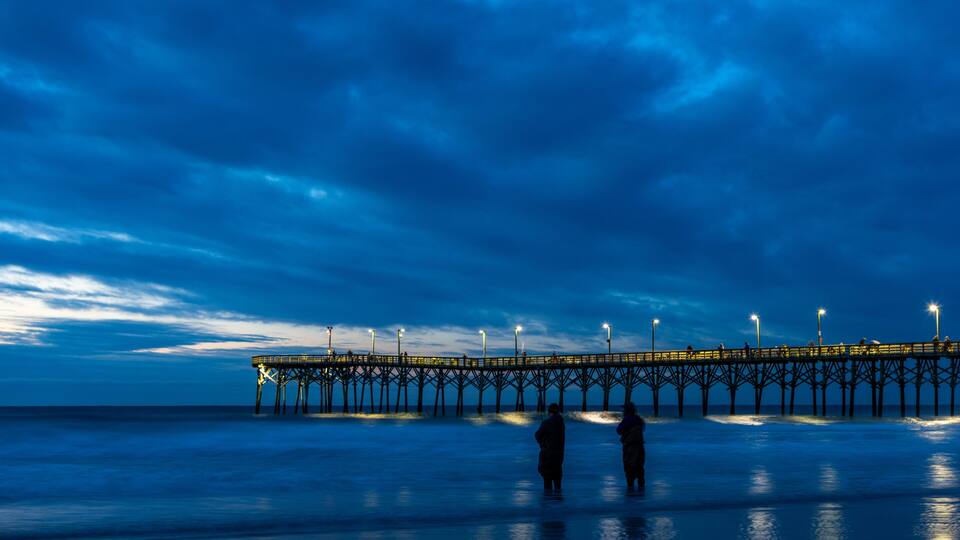 A pier extending into the water at dusk with people standing at the end.