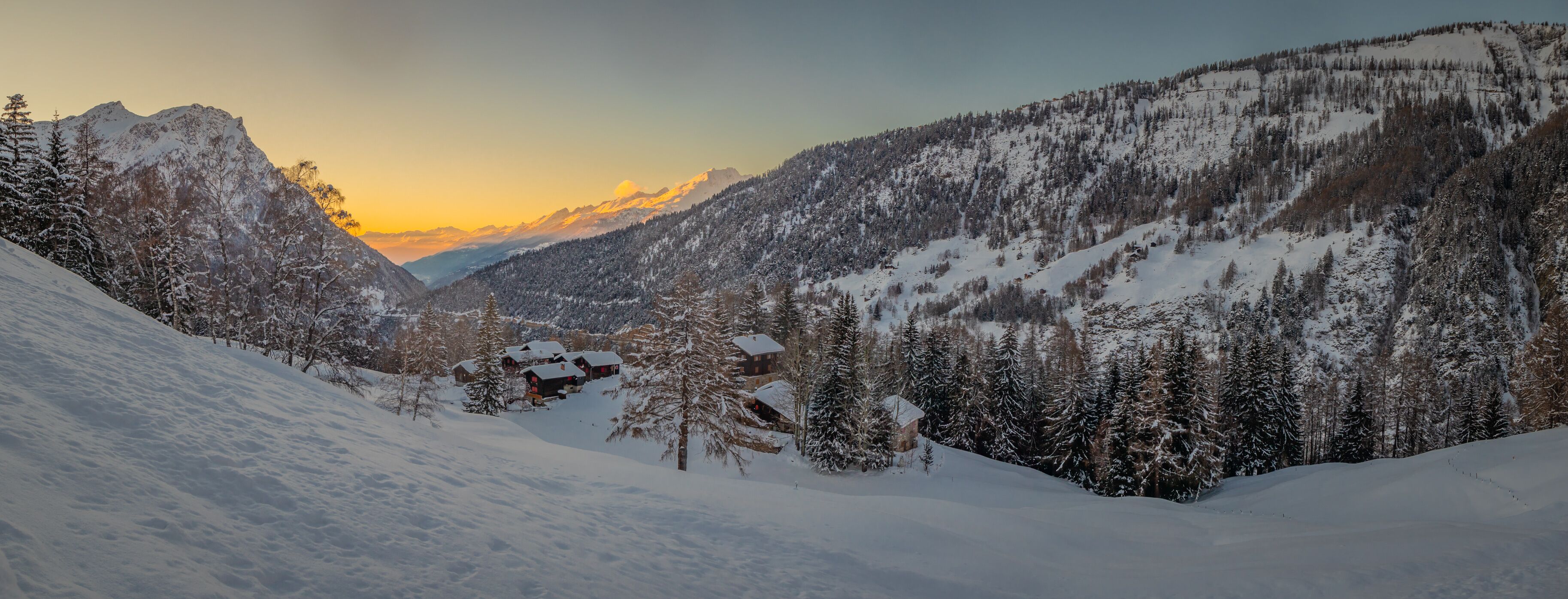 Romantic winter setting panorama of village in the alps close to Simplon pass in switzerland looking down towards Brig Valley covered in snow with beautiful sunset visible in the background.