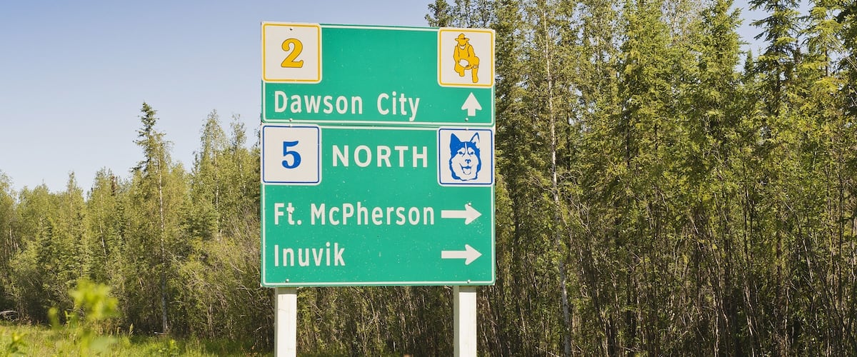 A directional road sign with arrows pointing to Dawson City, North, and Ft. McPherson.