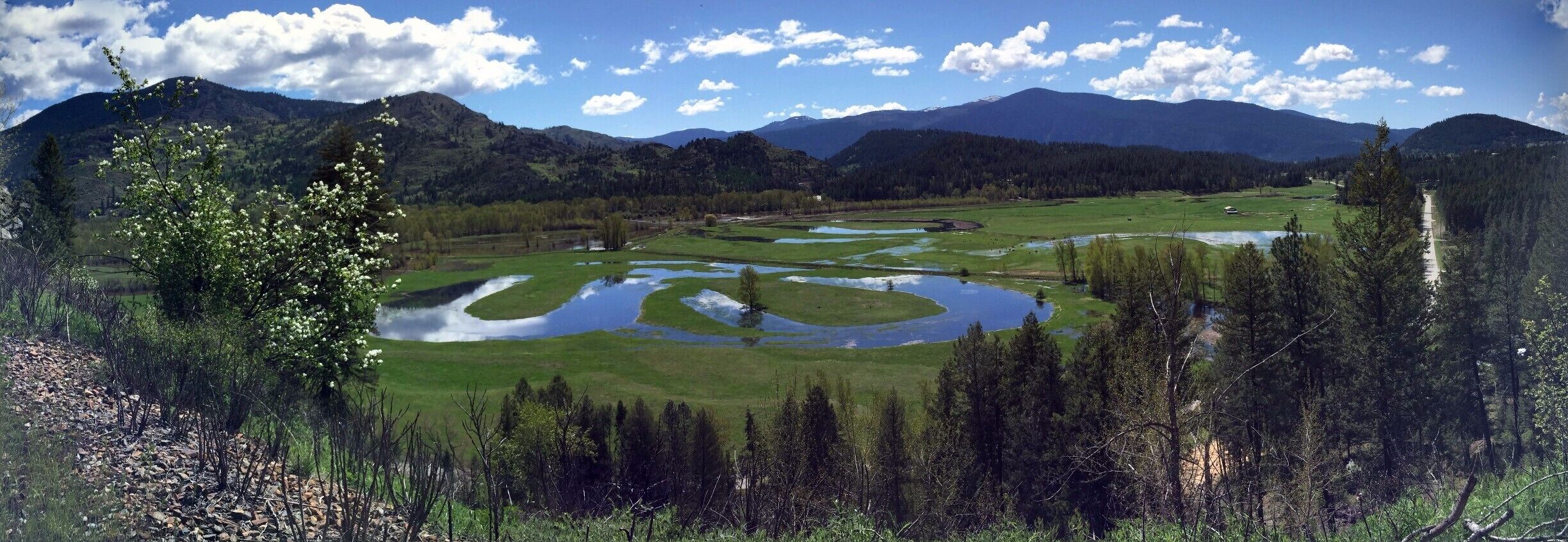 A landscape with a winding river, green fields, and mountains in the background.