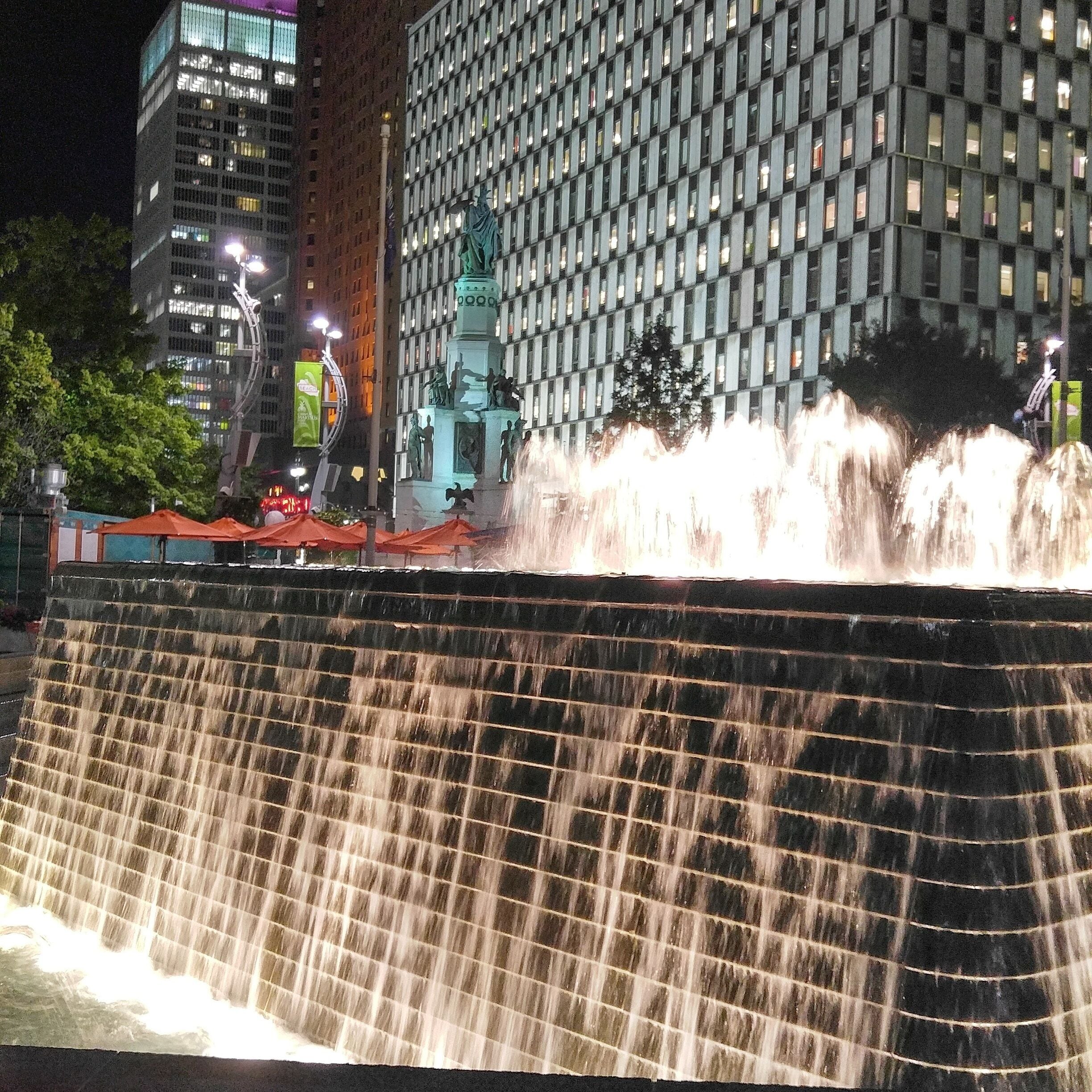 A nighttime waterfall feature with a statue in the background.