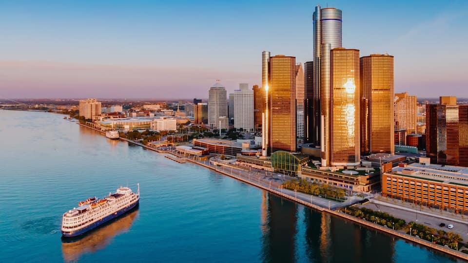 A river with a cruise ship, a city skyline with modern skyscrapers, and a clear sky.