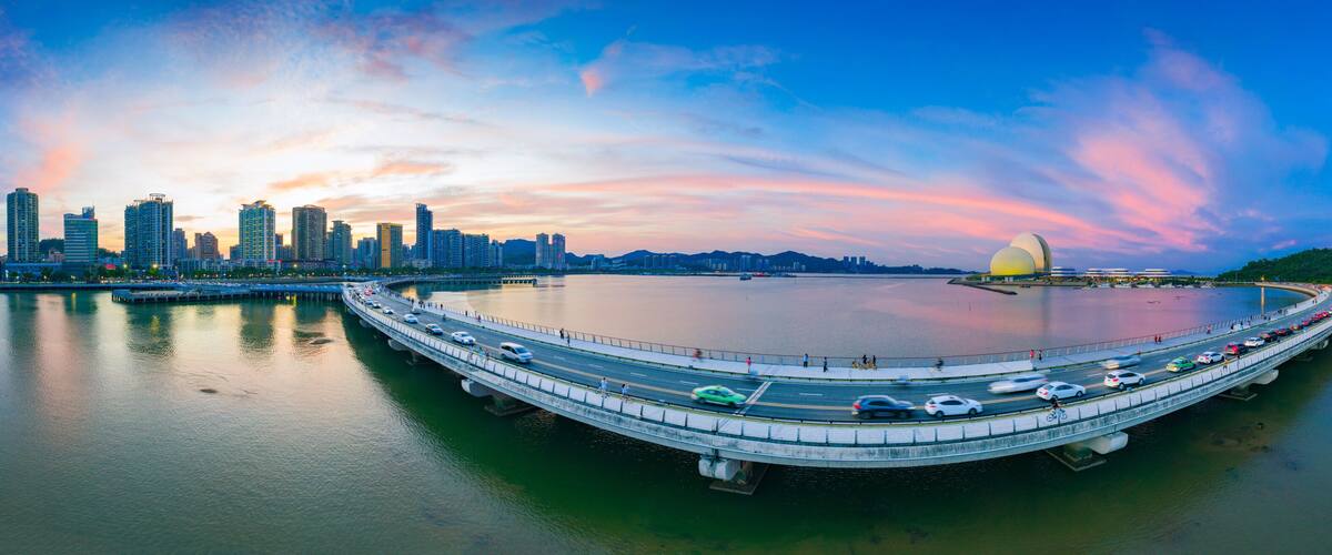 A city skyline with modern high-rises, a large circular water feature, and a traditional building with a red roof.