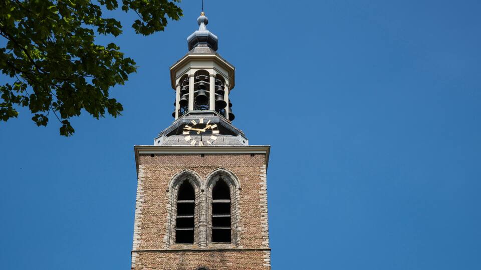 A tall brick tower with a clock and a spire against a clear blue sky.