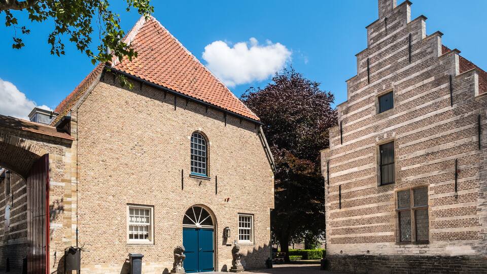 A historic building with a red-tiled roof and a blue door, surrounded by brick structures and a clear blue sky.