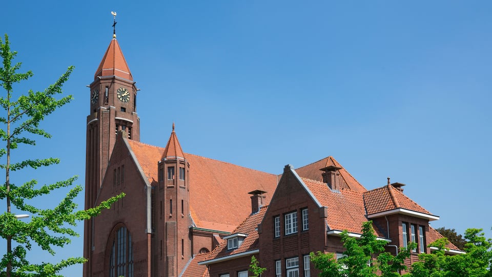 A red brick church with a clock tower and a steeple under a clear blue sky.