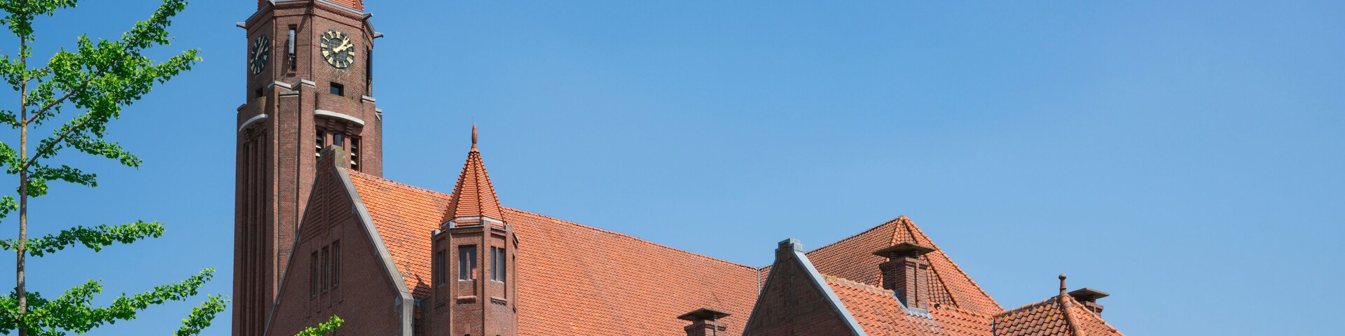 Igreja de tijolos vermelhos com uma torre do relógio e um pináculo sob um céu azul claro.