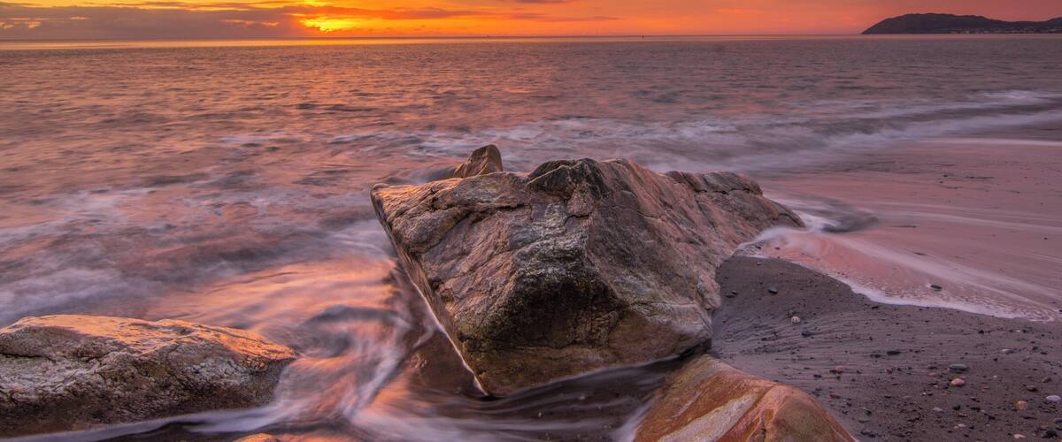 A sunset over the ocean with a rocky foreground.