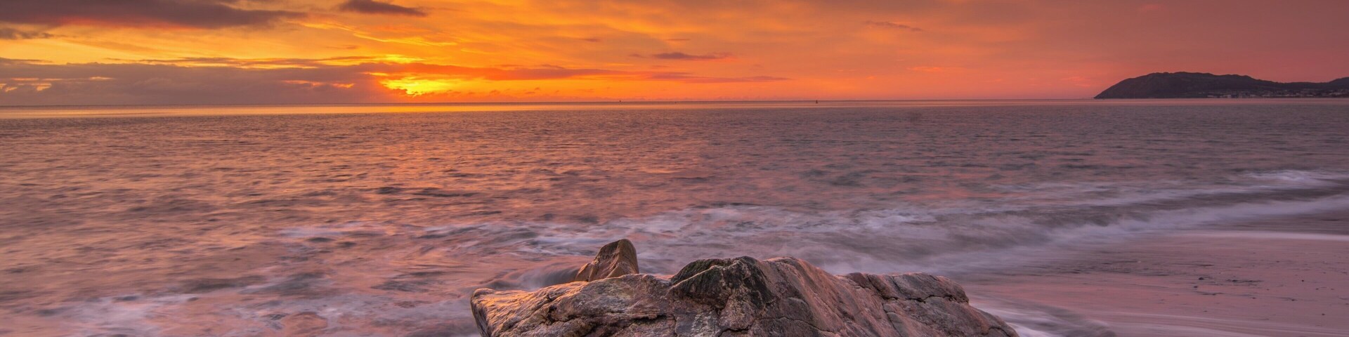 A sunset over the ocean with a rocky foreground.
