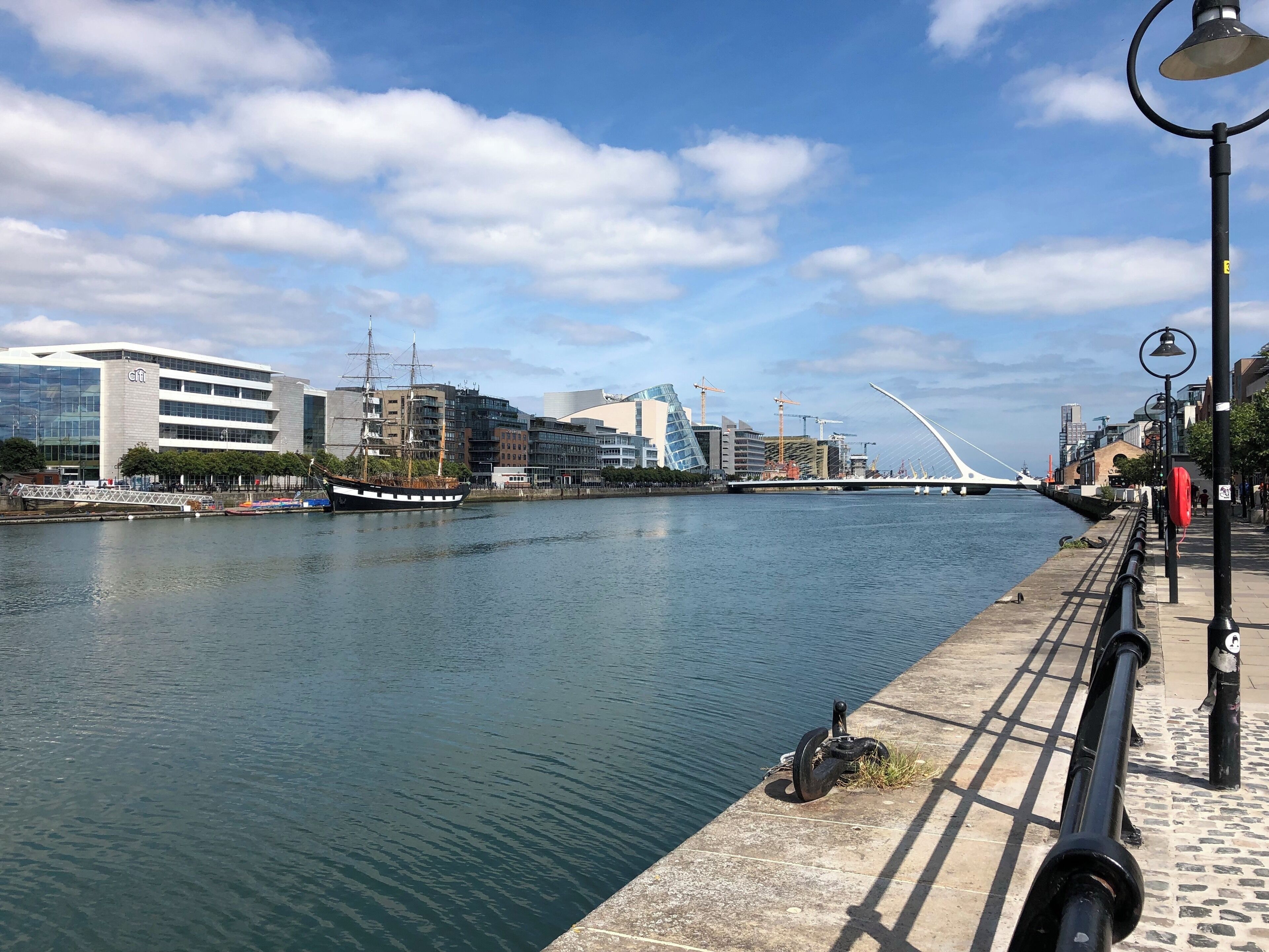Un río con un puente moderno, un barco de gran altura y un paisaje urbano con edificios y grúas de construcción.