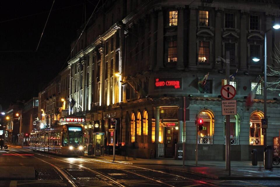 A tram on a wet street at night with illuminated buildings and a 'Grand Central' sign.