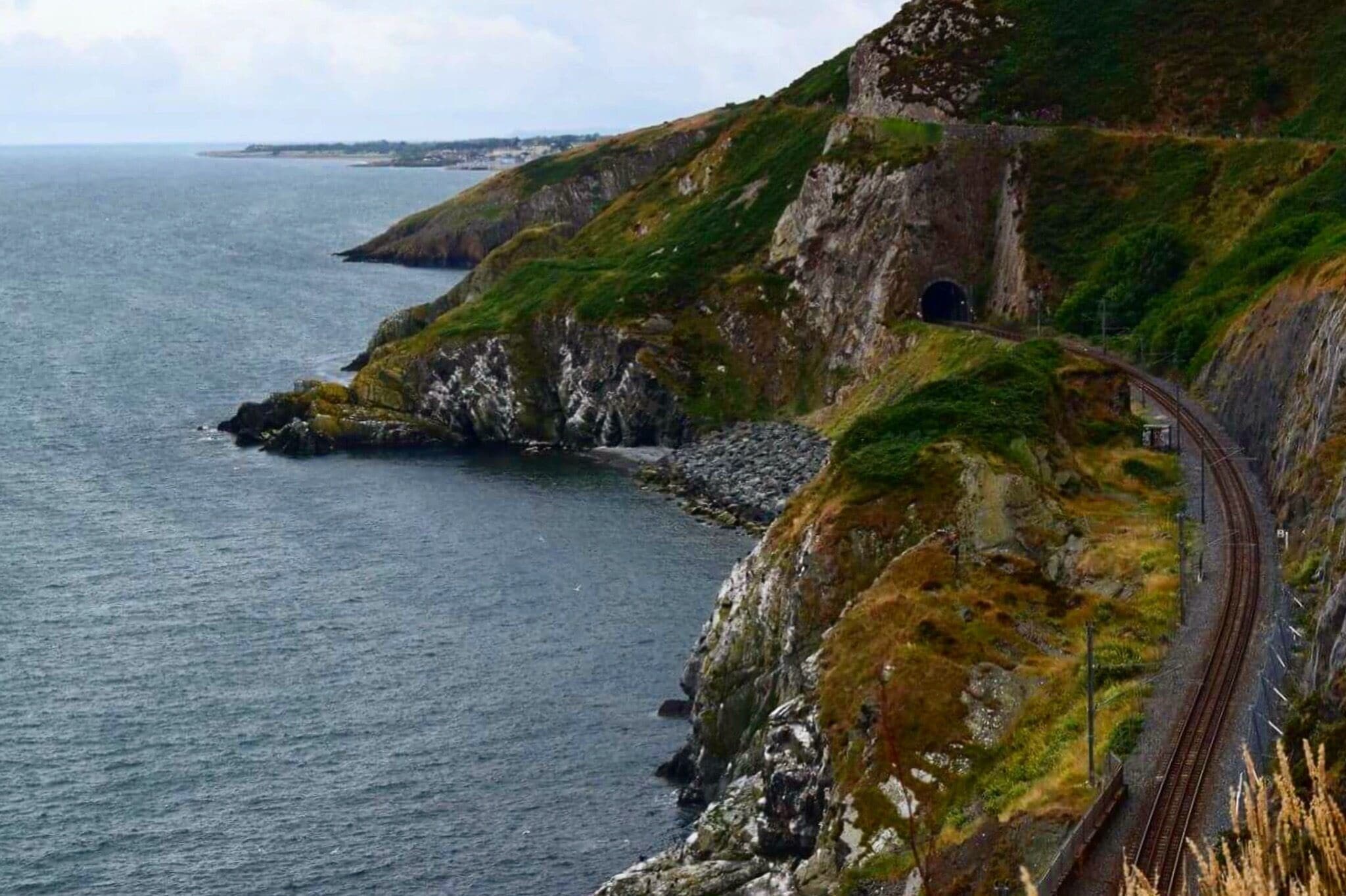 A coastal railway track curving along a cliffside with a tunnel entrance.