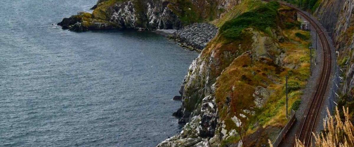 A coastal railway track curving along a cliffside with a tunnel entrance.