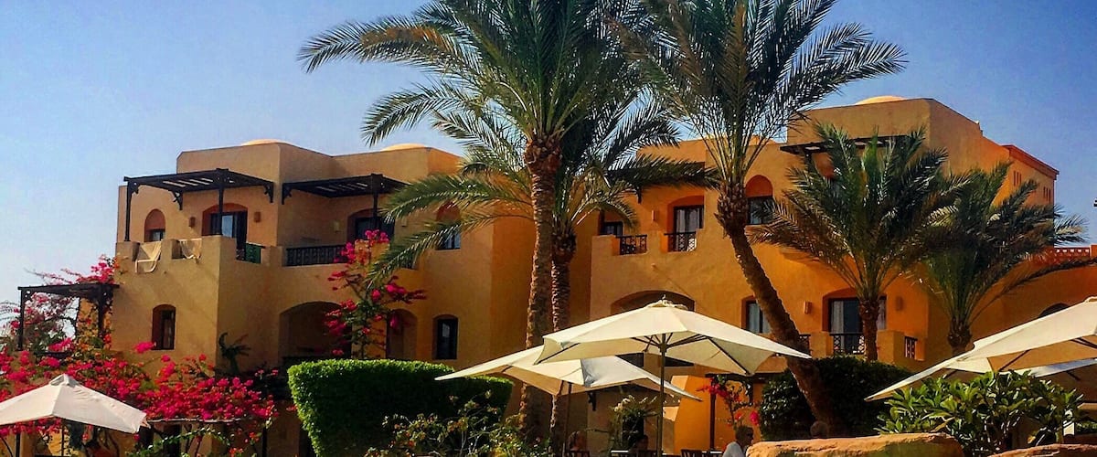 A pool with clear blue water, surrounded by palm trees and a building with arches.