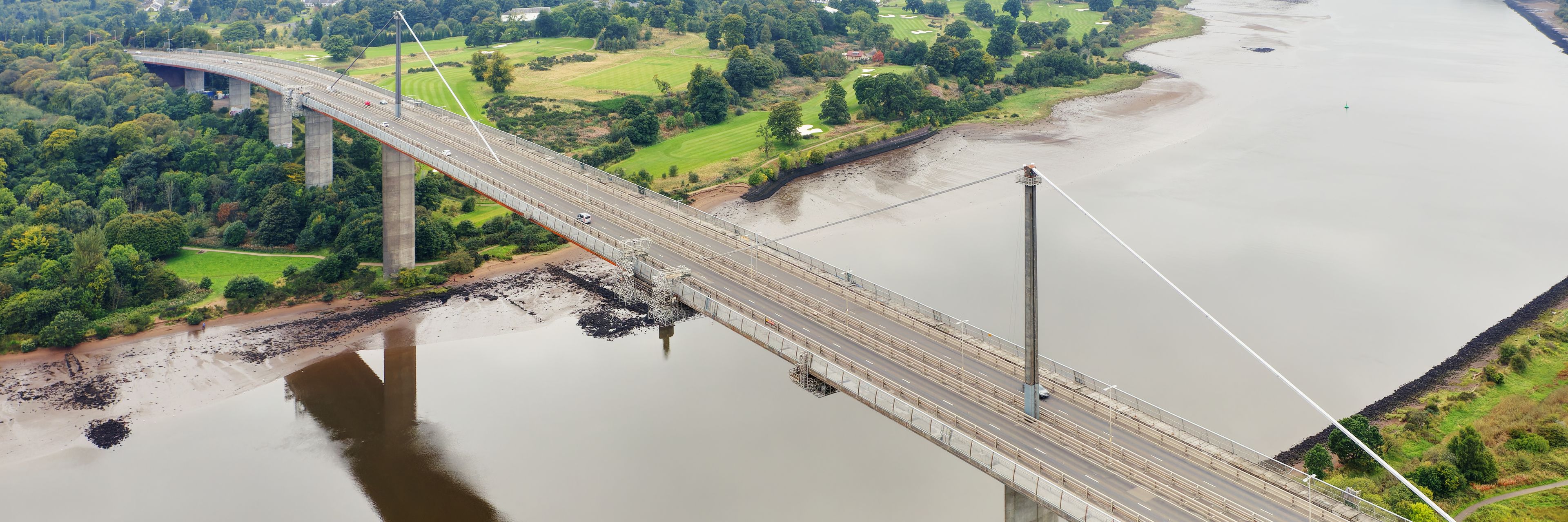 A bridge over a river with surrounding greenery and a golf course.