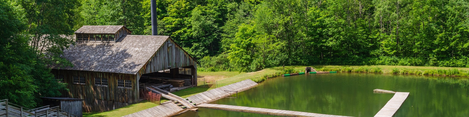 Un edificio de madera rústico cerca de un estanque con muelle, rodeado de un bosque verde exuberante.