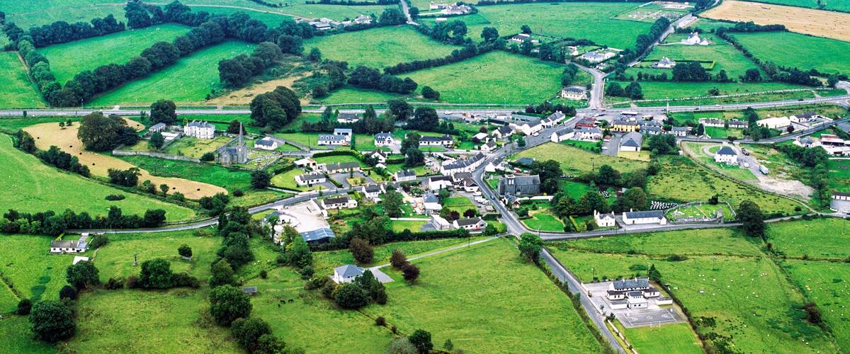 An aerial view of a rural village with green fields, scattered houses, and a prominent church.