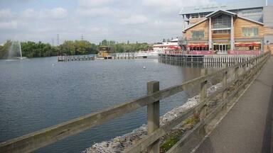A riverside walkway with a wooden fence, a bridge, and a building with a restaurant.
