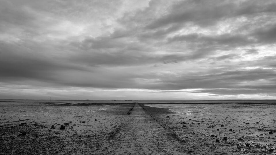 A deserted beach with a long, straight path leading to the horizon under a cloudy sky.