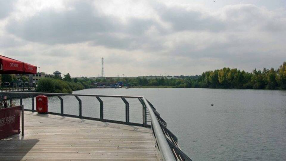 A wooden pier with a railing, a red sign, and a calm river with trees in the background.