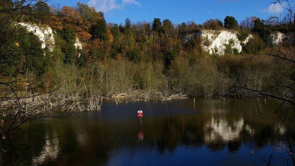 A calm lake with a red buoy, surrounded by autumn-colored trees and cliffs.
