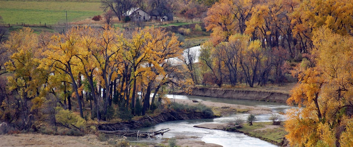 A river winding through a landscape with autumn-colored trees and a small house in the distance.
