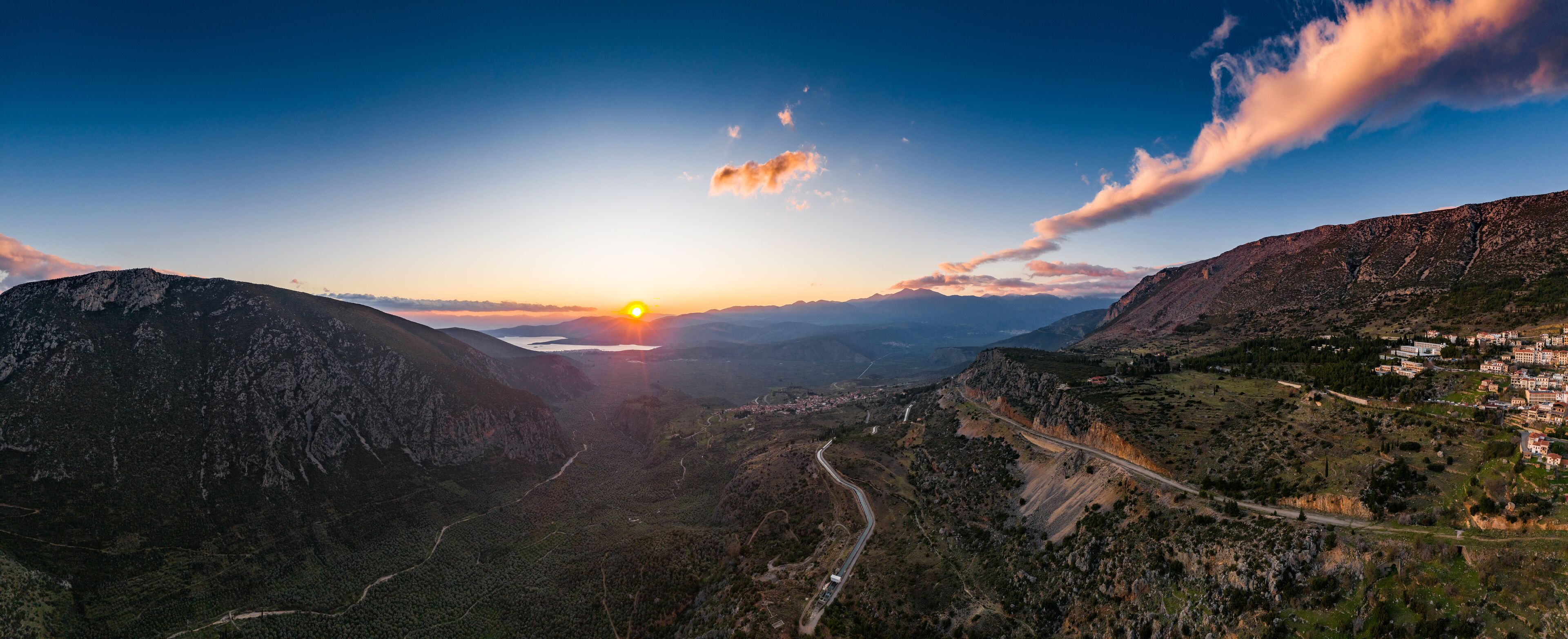 Aerial view of Delphi, Greece, the Gulf of Corinth, orange color of clouds, mountainside with layered hills beyond with rooftops in foreground