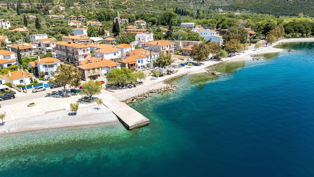 A coastal town with terracotta-roofed buildings, a clear blue sea, and a rocky shoreline.