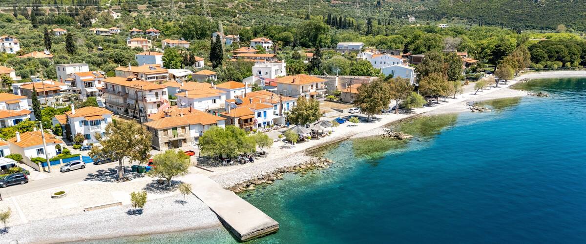 A coastal town with terracotta-roofed buildings, a clear blue sea, and a rocky shoreline.