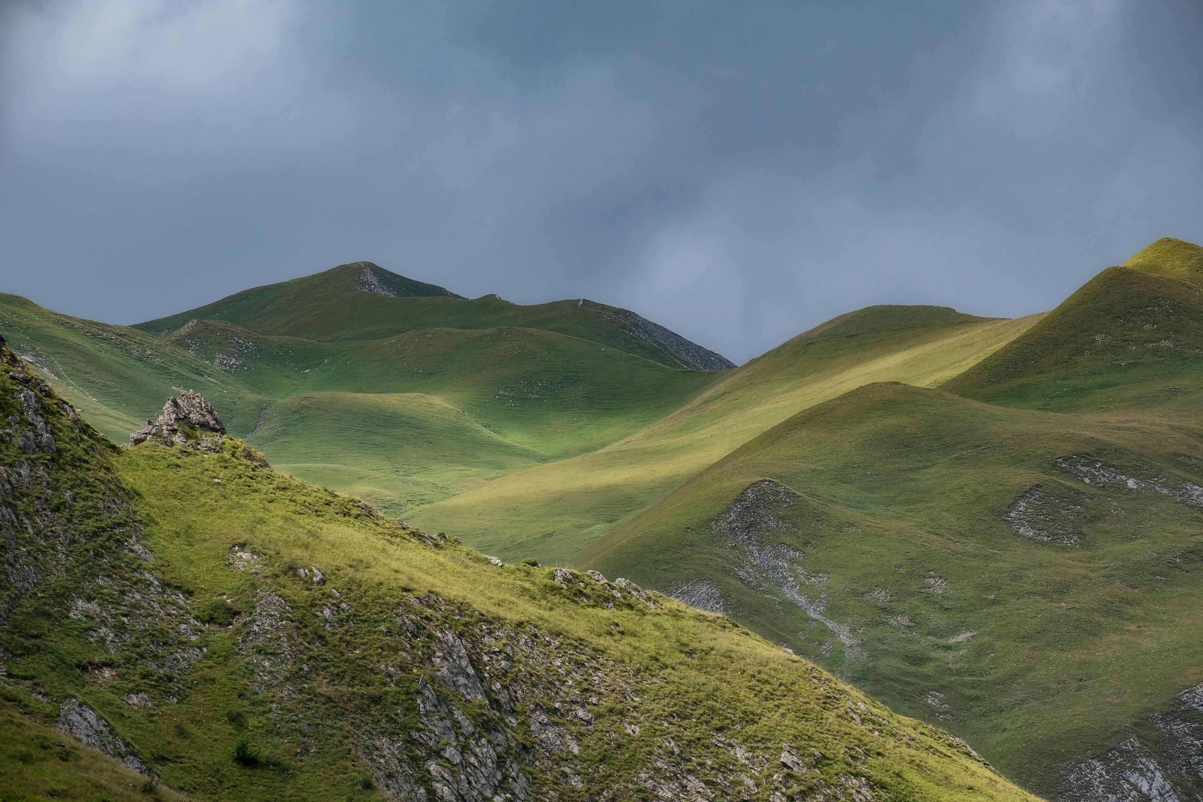 Rolling green hills with rocky outcrops under a cloudy sky.