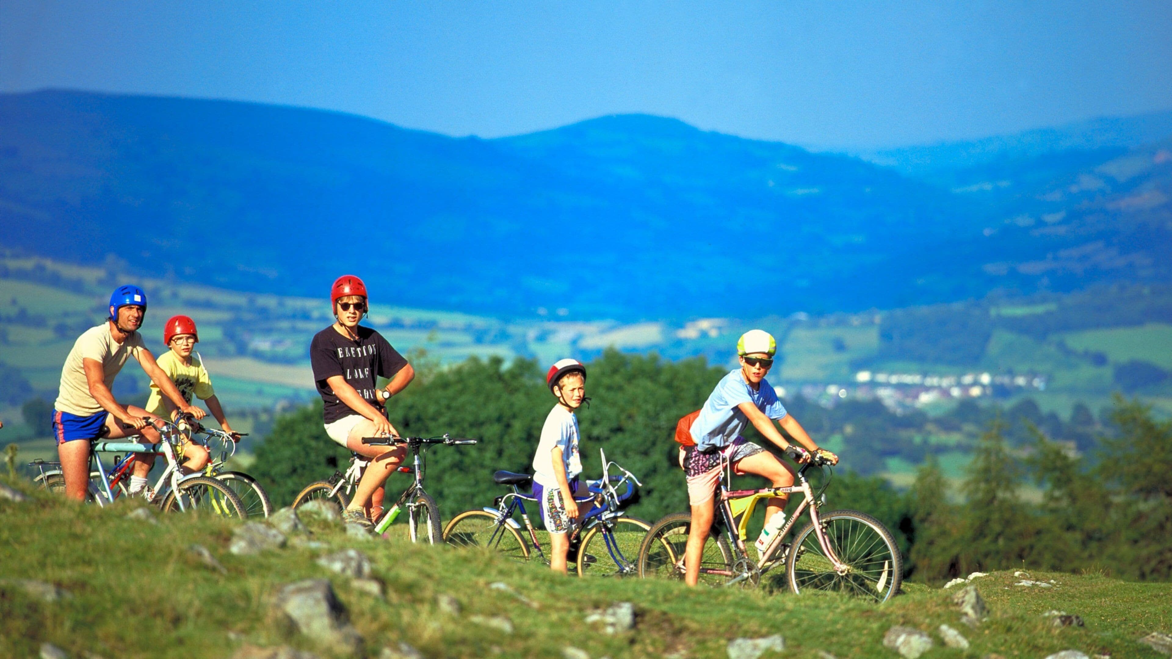 A group of cyclists on a grassy hill with a mountainous landscape in the background.